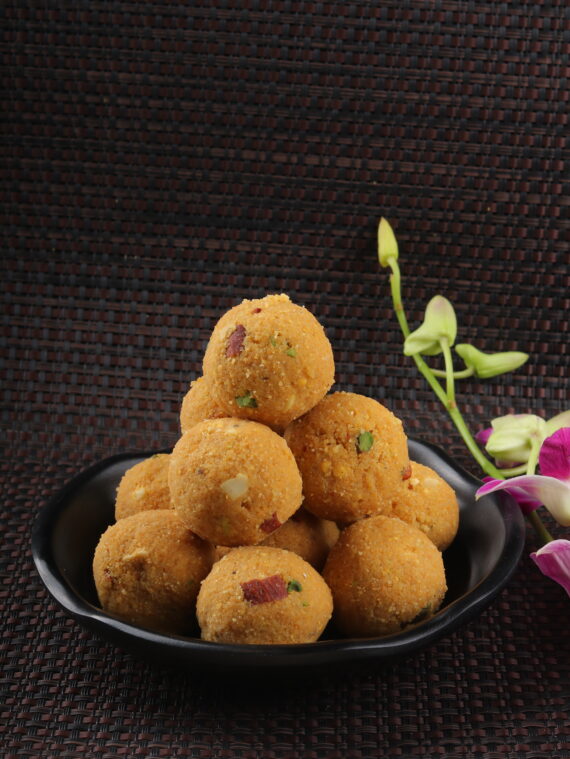 order dry fruit laddus, round sweets made from roasted gram flour and mixed with almonds, cashews, and raisins, presented on a brass plate with scattered dry fruits.