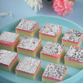 Slices of Pink Coconut Burfi, a pink-colored Indian sweet with coconut flavor, garnished with shredded coconut, arranged on a decorative plate.