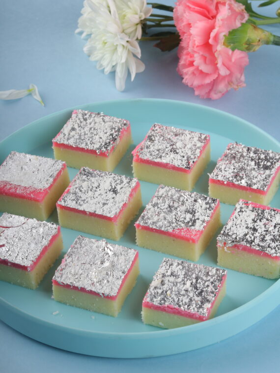 Slices of Pink Coconut Burfi, a pink-colored Indian sweet with coconut flavor, garnished with shredded coconut, arranged on a decorative plate.
