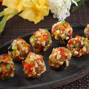 late of mix dry fruit laddus packed with assorted nuts and dried fruits, placed on a rustic wooden table with a bowl of mixed nuts and dried fruits beside it.