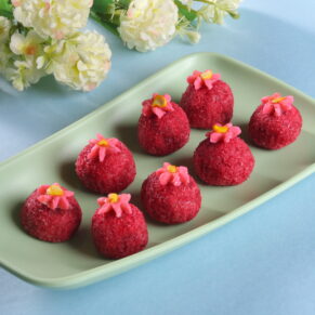 Plate of paan dry fruit laddus infused with betel leaf flavor, decorated with edible silver foil and dried rose petals, placed on a brass plate.